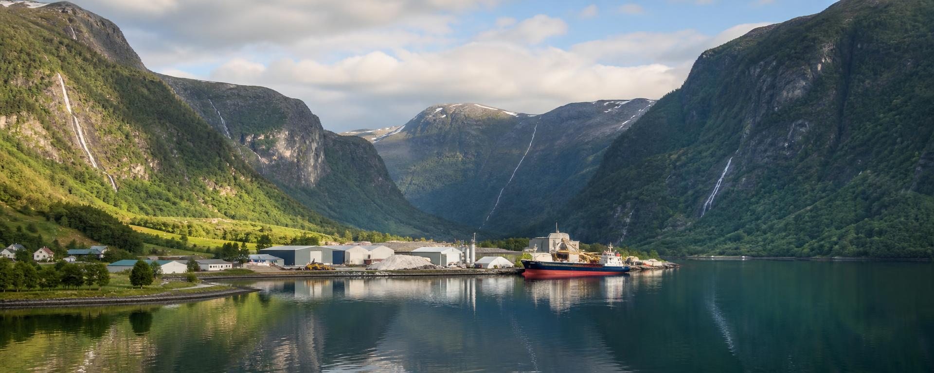 Industriområde med kai og lasteskip innerst i en vestlandsfjord.